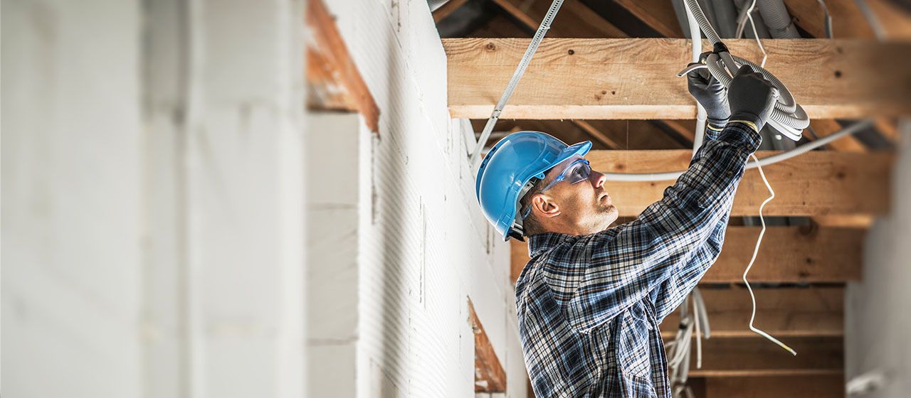 A contractor in a hard hat running cable in a new construction building