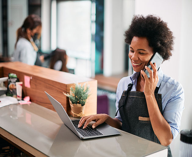 A salon manager talking on the phone while updating employee shifts on a laptop