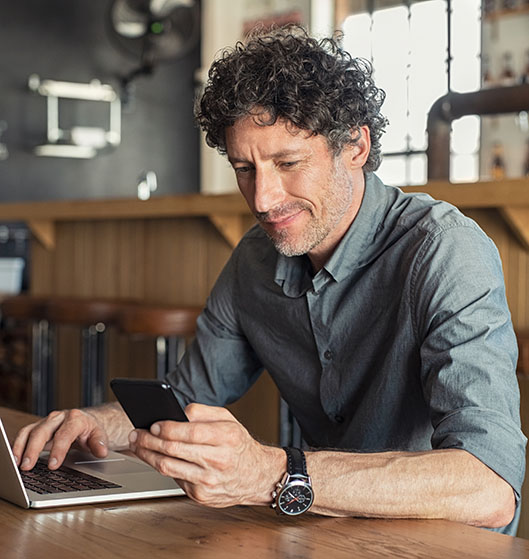 A man reviewing business performance on his laptop and iPhone using North's merchant portal services