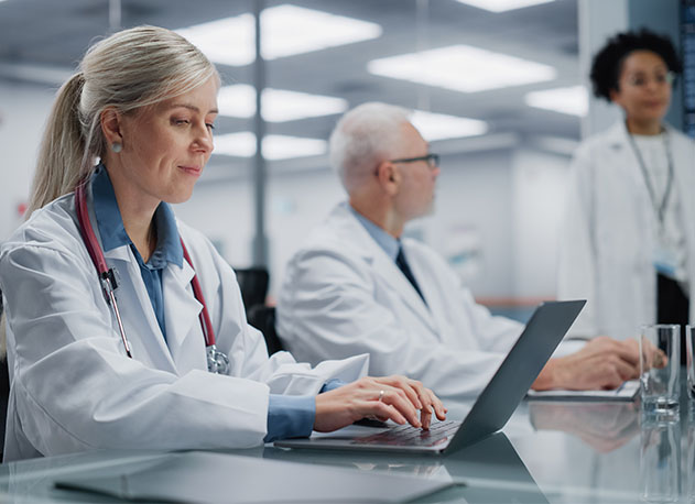 A doctor on her laptop sitting next to other doctors in a glass room